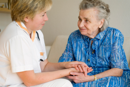 Nurse is sitting in front of the patient holding her hands and looking at each other face to face.