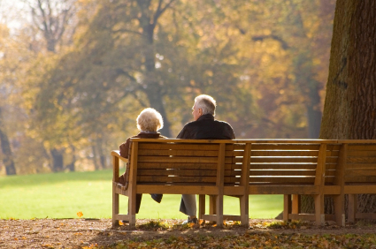 Older couple sitting on a wooden bench in a park.